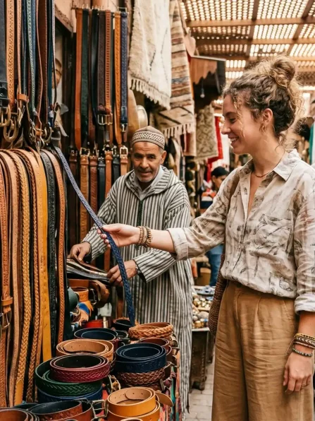 Young woman browsing through a vibrant selection of handmade leather belts in a traditional Moroccan souk in Marrakech, immersed in local