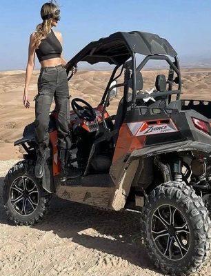 Two people driving a 1000cc buggy through the Agafay Desert with rocky trails and the Atlas Mountains in the background